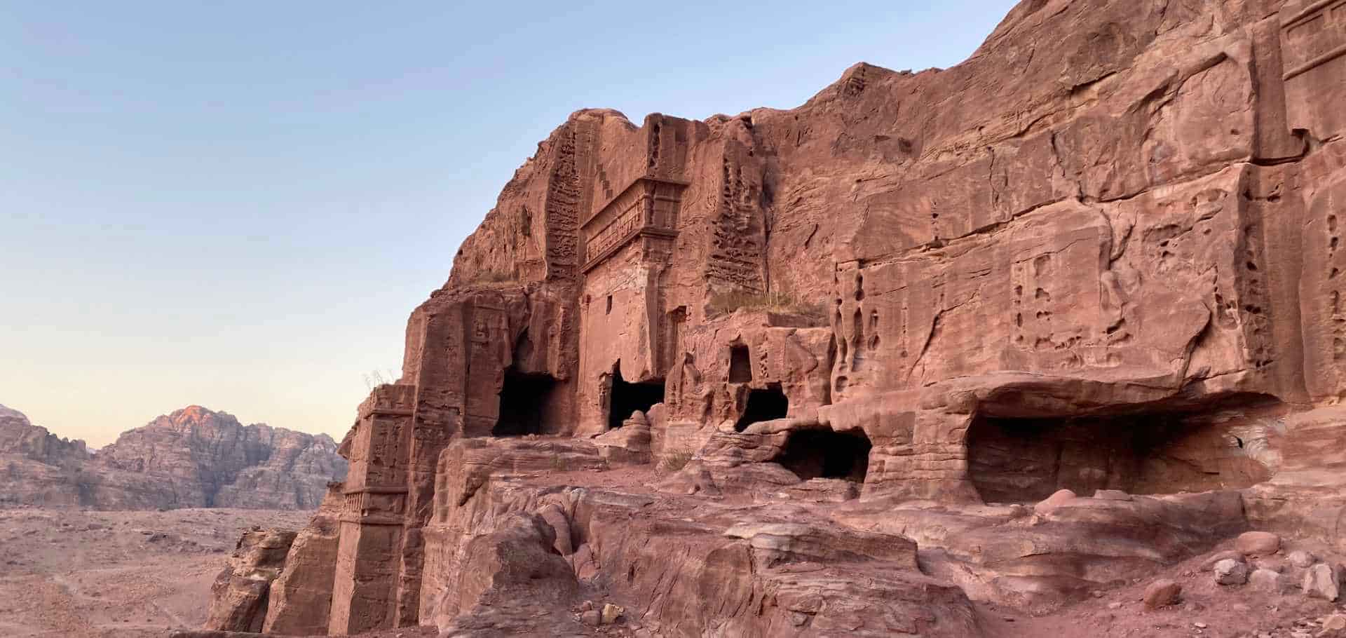 Weathered cave dwellings and ancient rock-cut tombs dotting the rugged Jordanian canyon landscape.