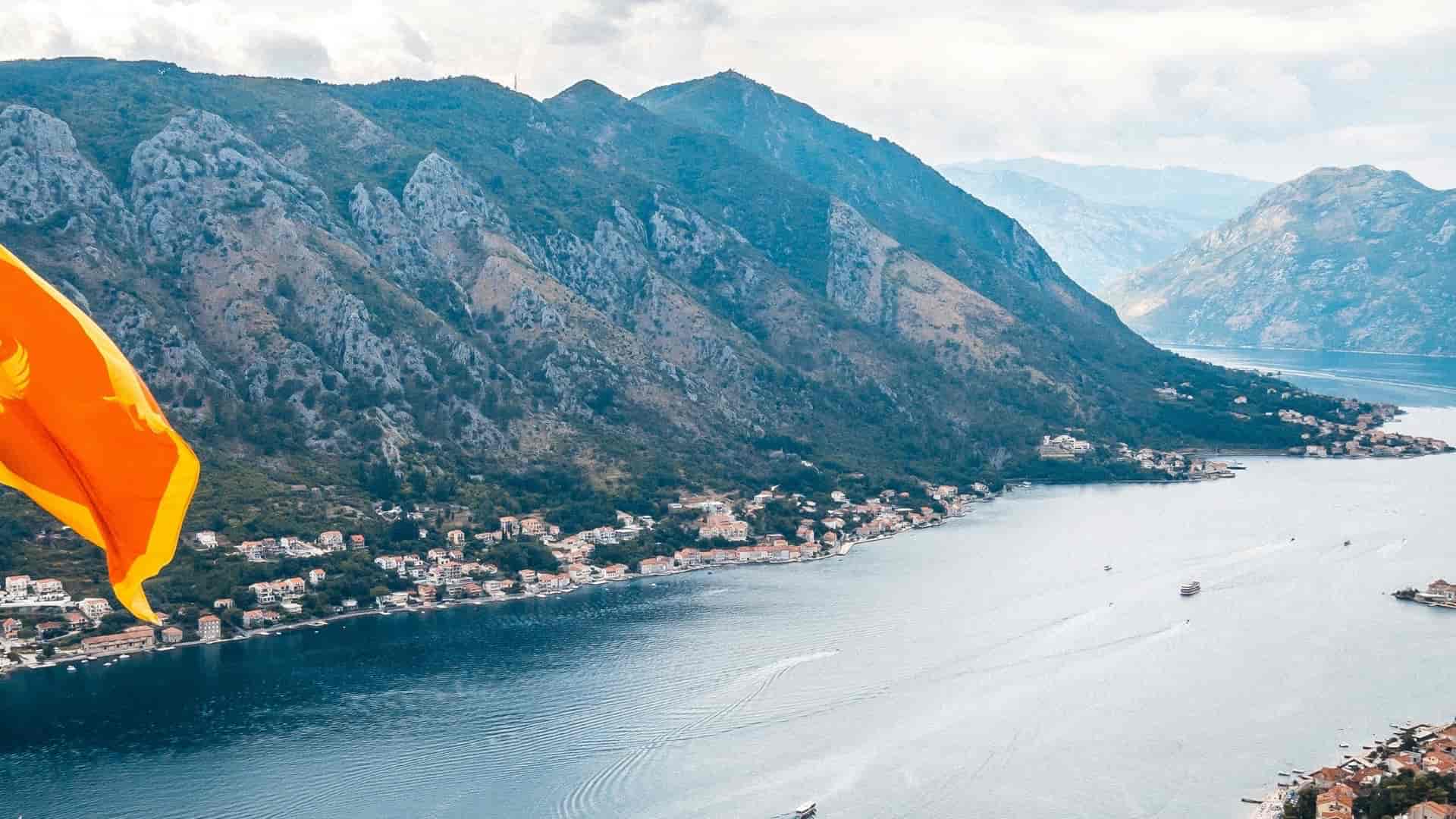 Montenegrin flag waving over a high-angle panoramic view of the Bay of Kotor.
