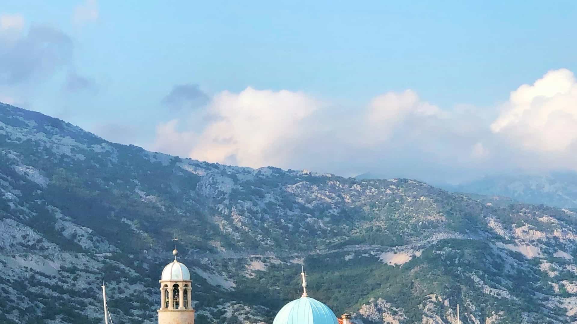 Venetian church dome and bell tower against steep green mountain slopes in Kotor.