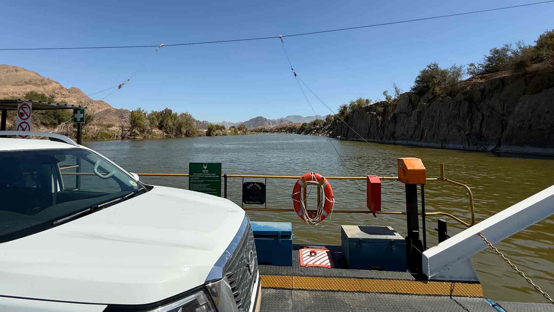 A white vehicle parked on a steel river pontoon crossing the muddy Orange River
