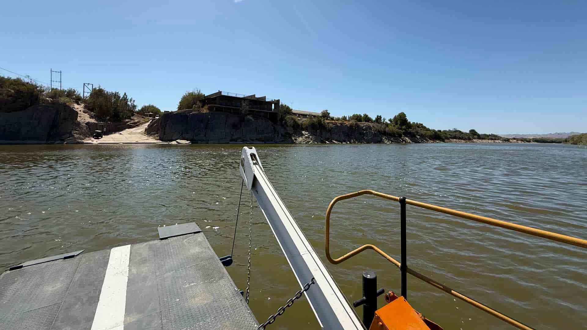 View from a moving steel pontoon looking toward the rocky Namibian riverbank.