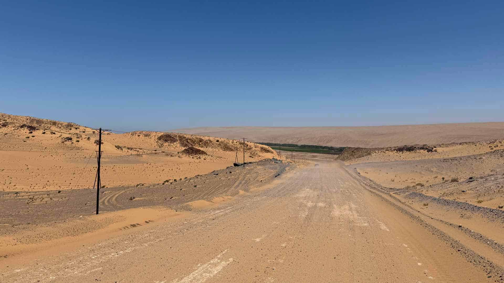 A dusty desert gravel road stretching through the arid mountainous landscape toward the horizon.