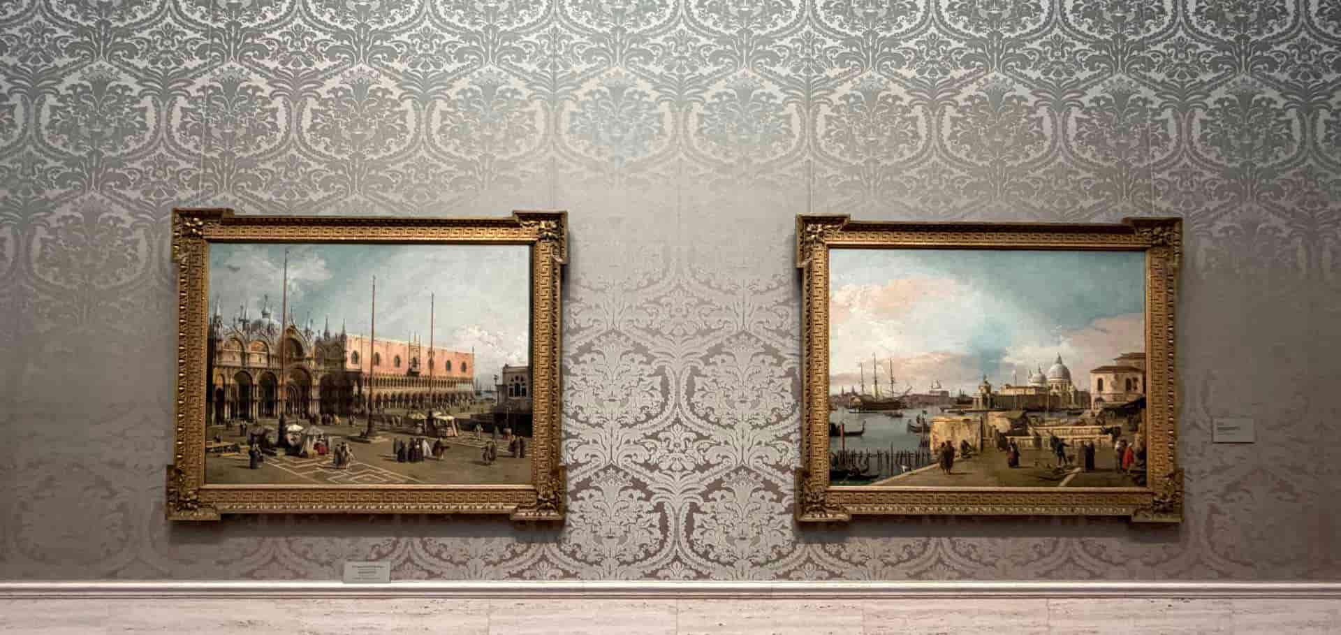 Two framed Venetian landscape paintings hang on an ornate damask patterned wall.