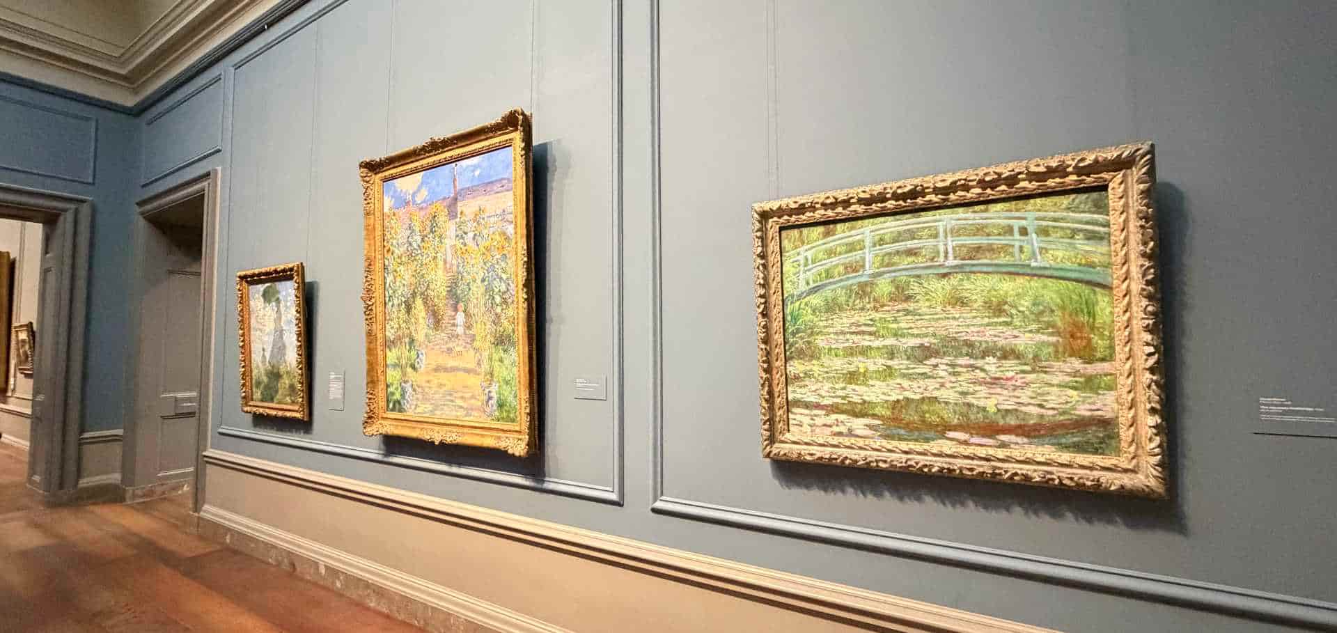 Impressionist paintings including Monet's water lilies hang along a grey gallery wall.