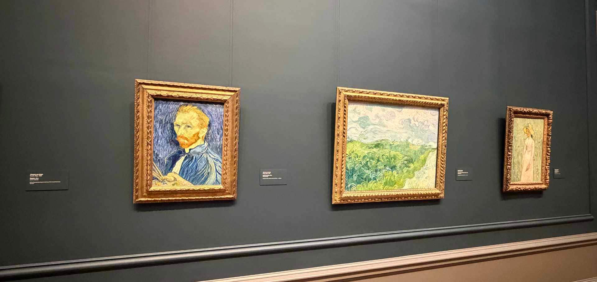 Vincent van Gogh's self-portrait and pastoral landscapes displayed on a dark grey wall.