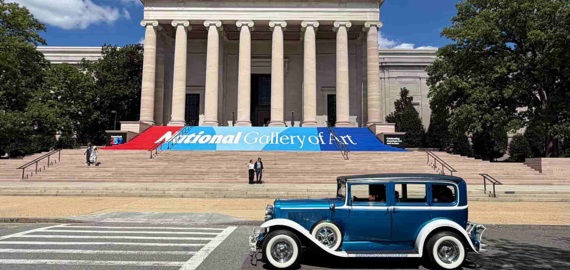 A vintage blue car parked in front of the grand neoclassical columns of the National Gallery of Art.