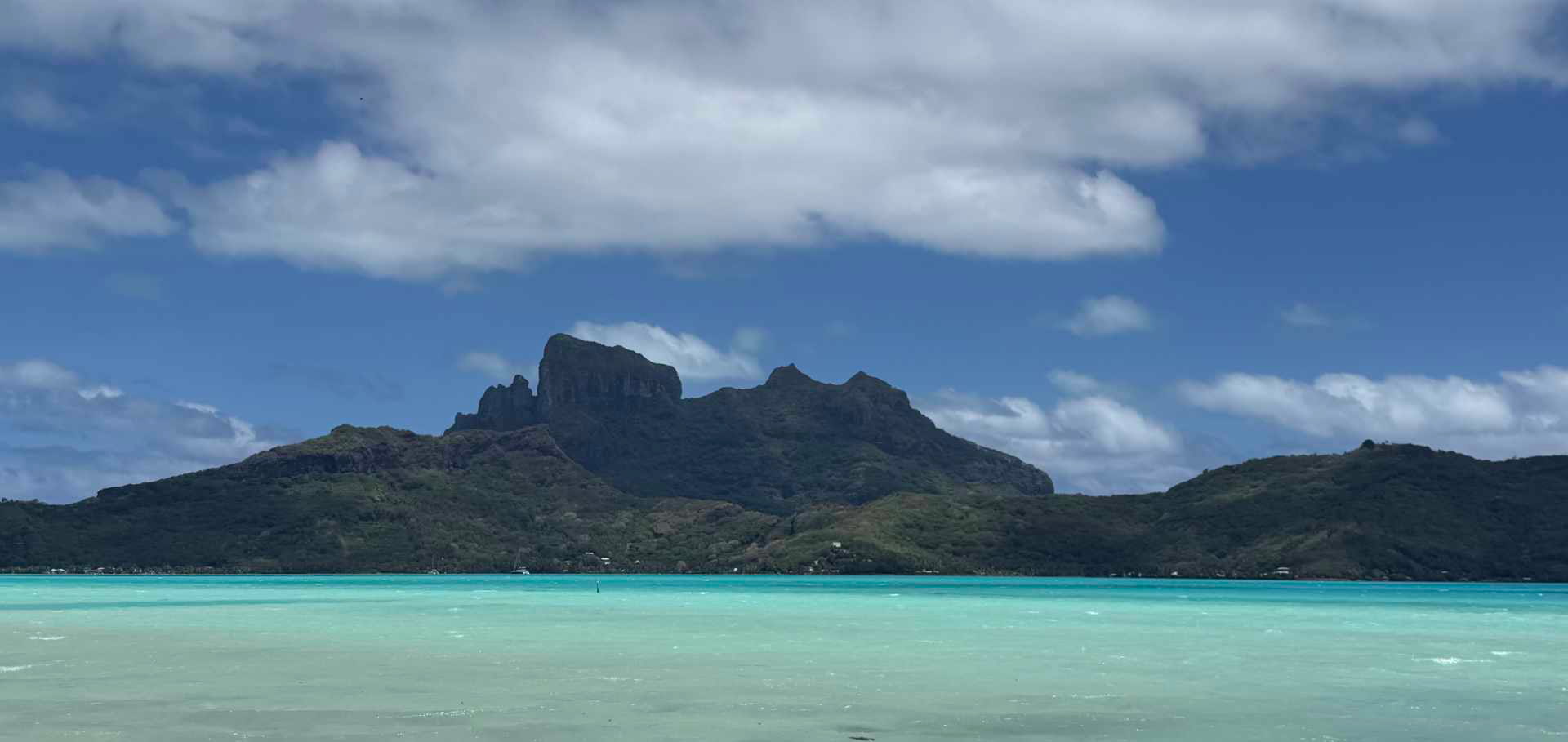 Rugged volcanic peak of Mount Otemanu under a bright blue sky with scattered white clouds.