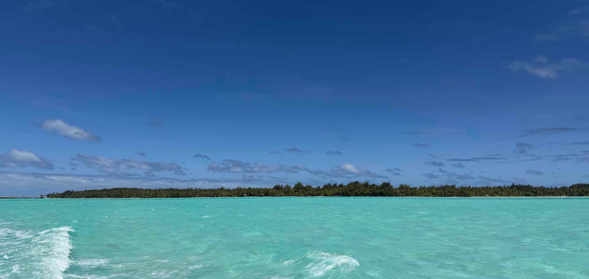 Bright turquoise ocean waters stretching toward a distant palm-fringed tropical island shore.