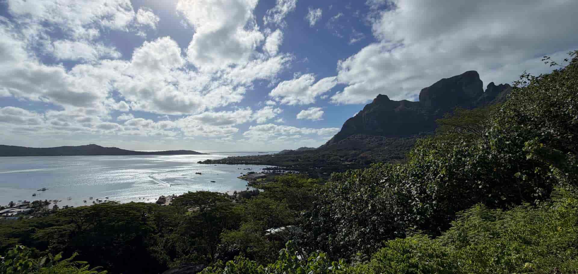 Panoramic view from a lush green ridge overlooking the tranquil coastal lagoon and distant islands.