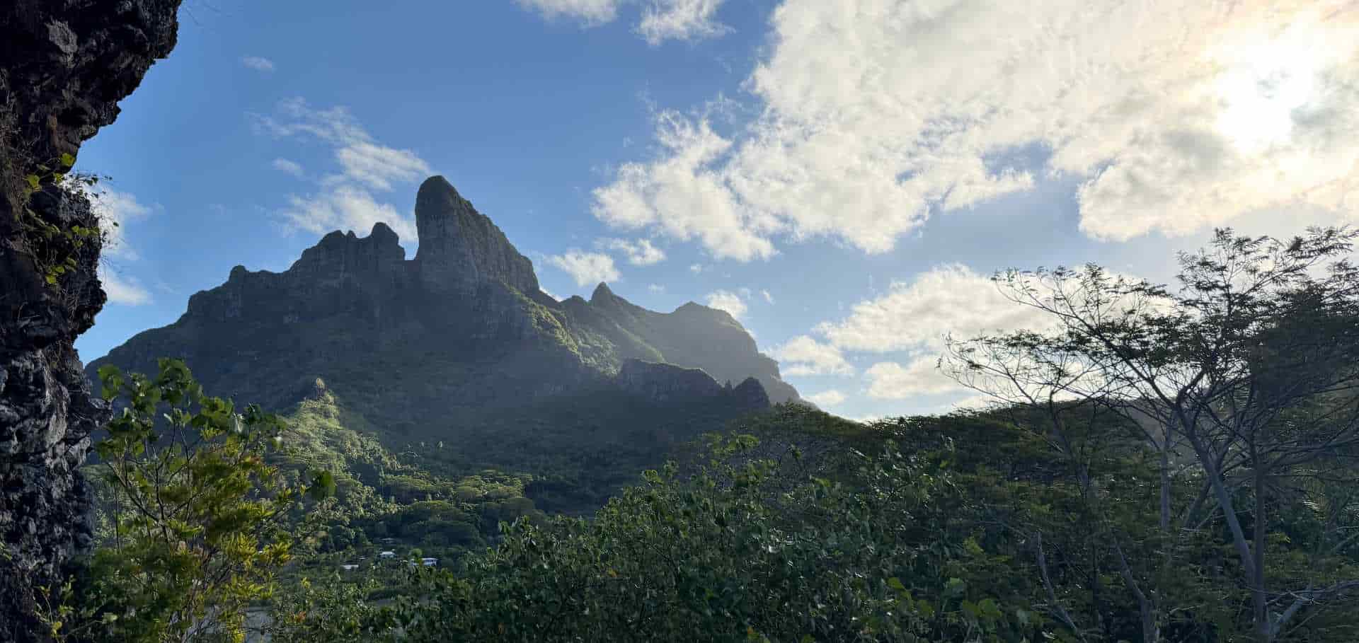 Dramatic basalt peaks of Mount Otemanu framed by lush green jungle foliage and blue skies.