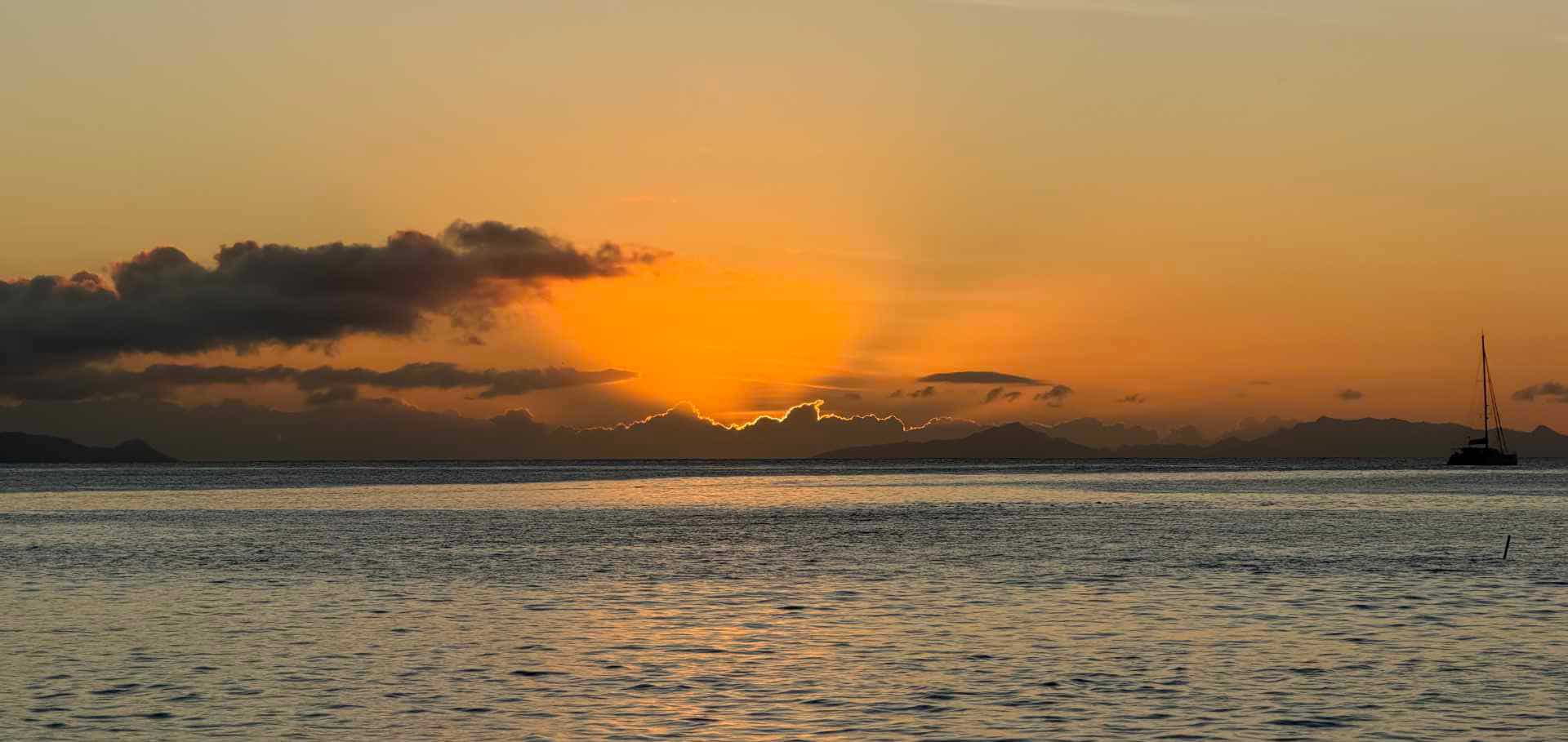 A serene sunset casts a warm orange glow across the rippling ocean waves and distant horizon.