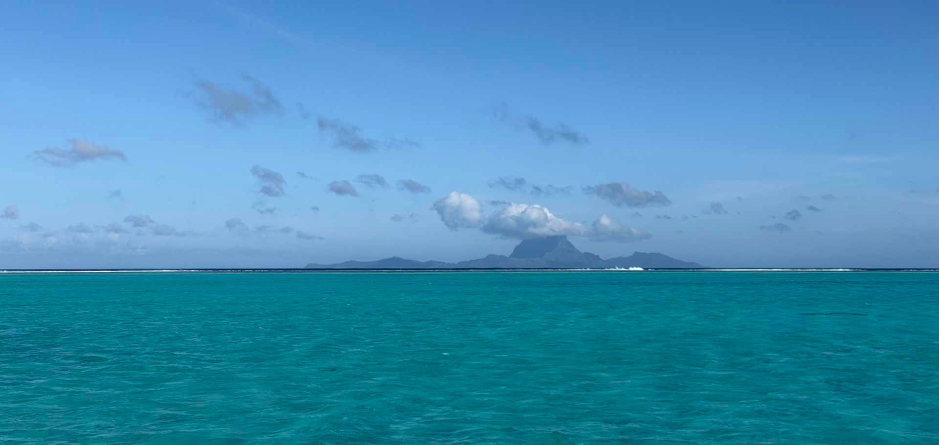 Distant volcanic island peaks rising above a vibrant turquoise ocean horizon.