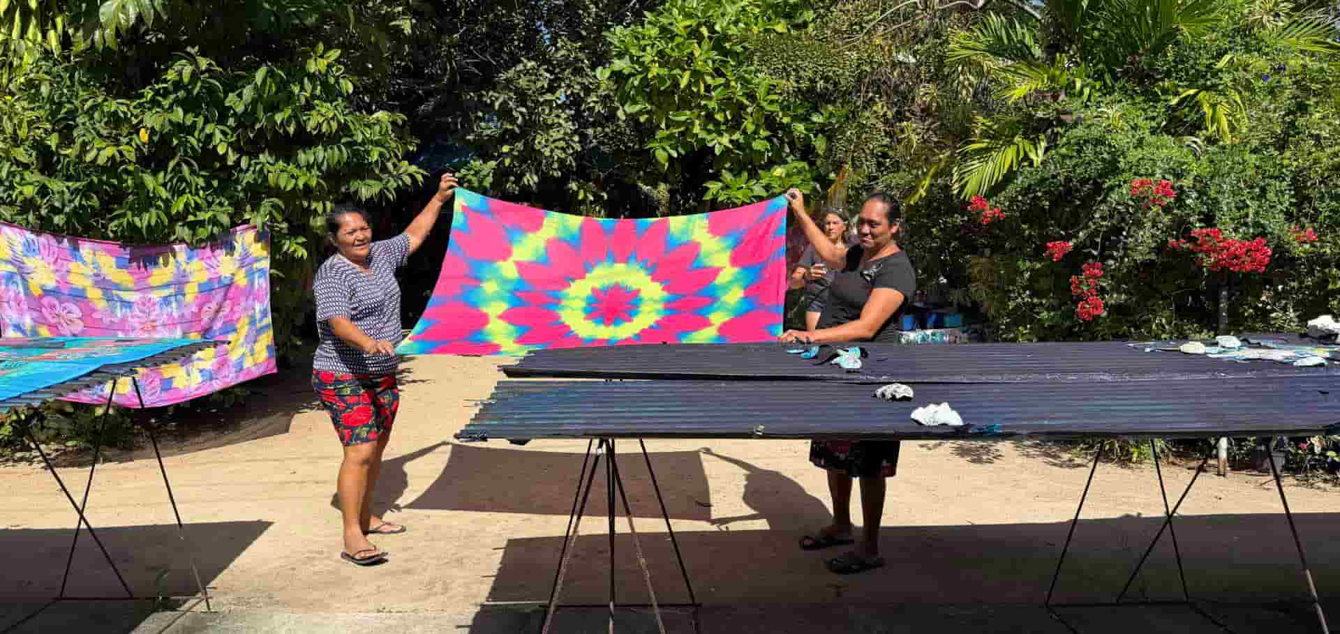 Artisans holding a brightly colored tie-dye fabric outside an open-air studio.