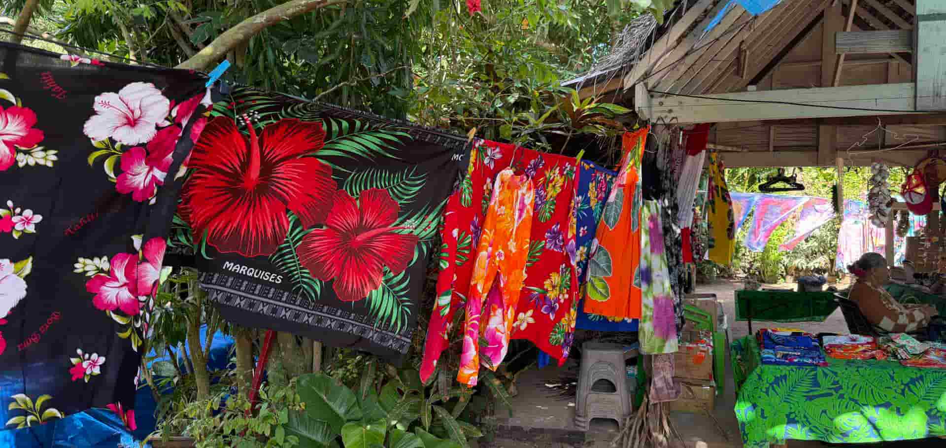 Traditional hand-dyed pareos and tropical garments displayed on racks outdoors.