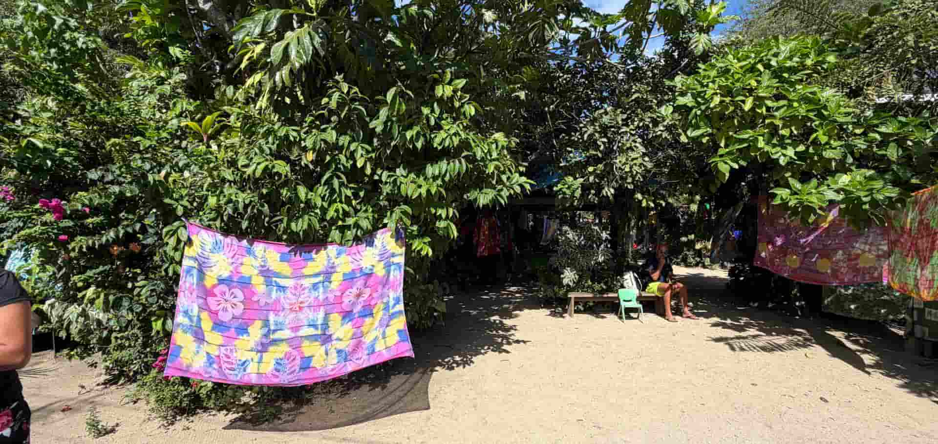 A vibrant pink and yellow hand-dyed pareo hanging in the tropical shade.