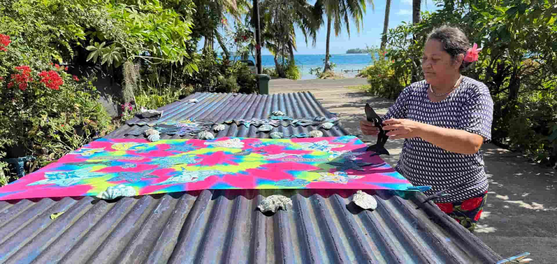 An artisan working with a brightly colored fabric stretched across outdoor tables.