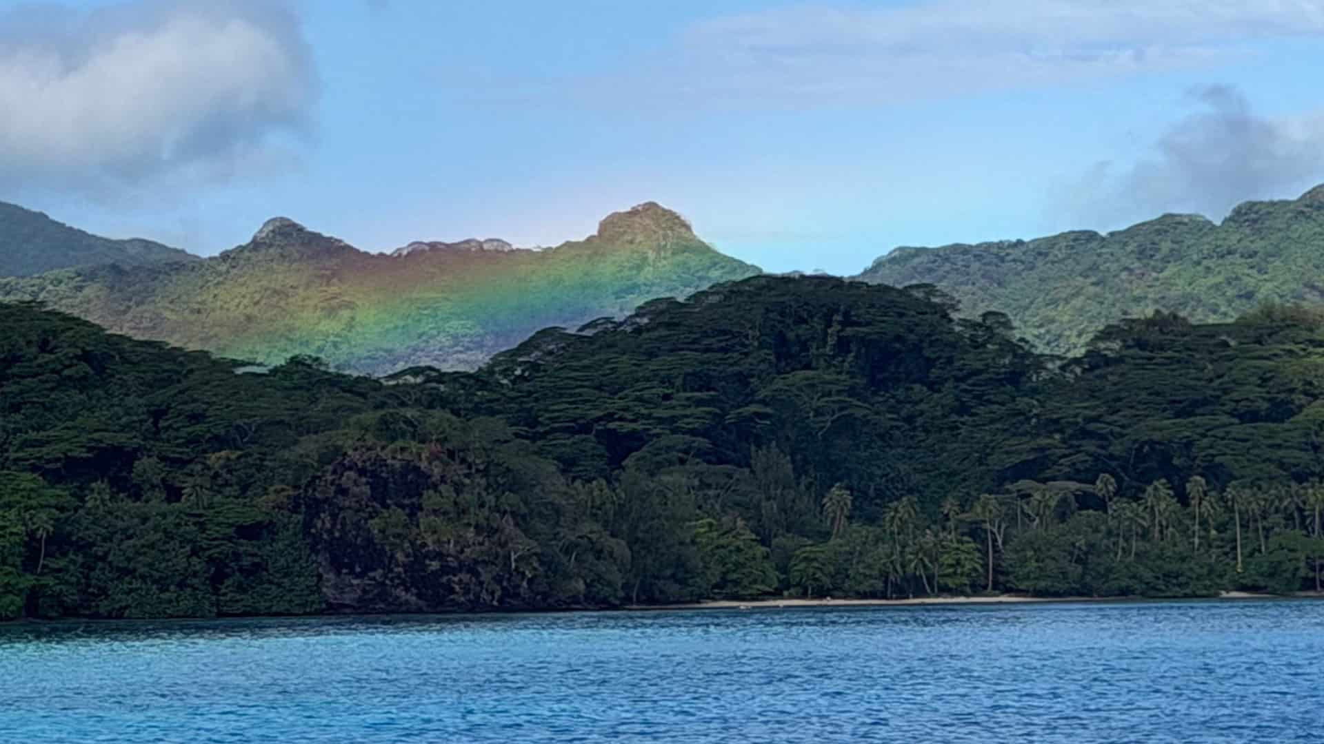 Faint rainbow arching across lush green volcanic peaks in French Polynesia