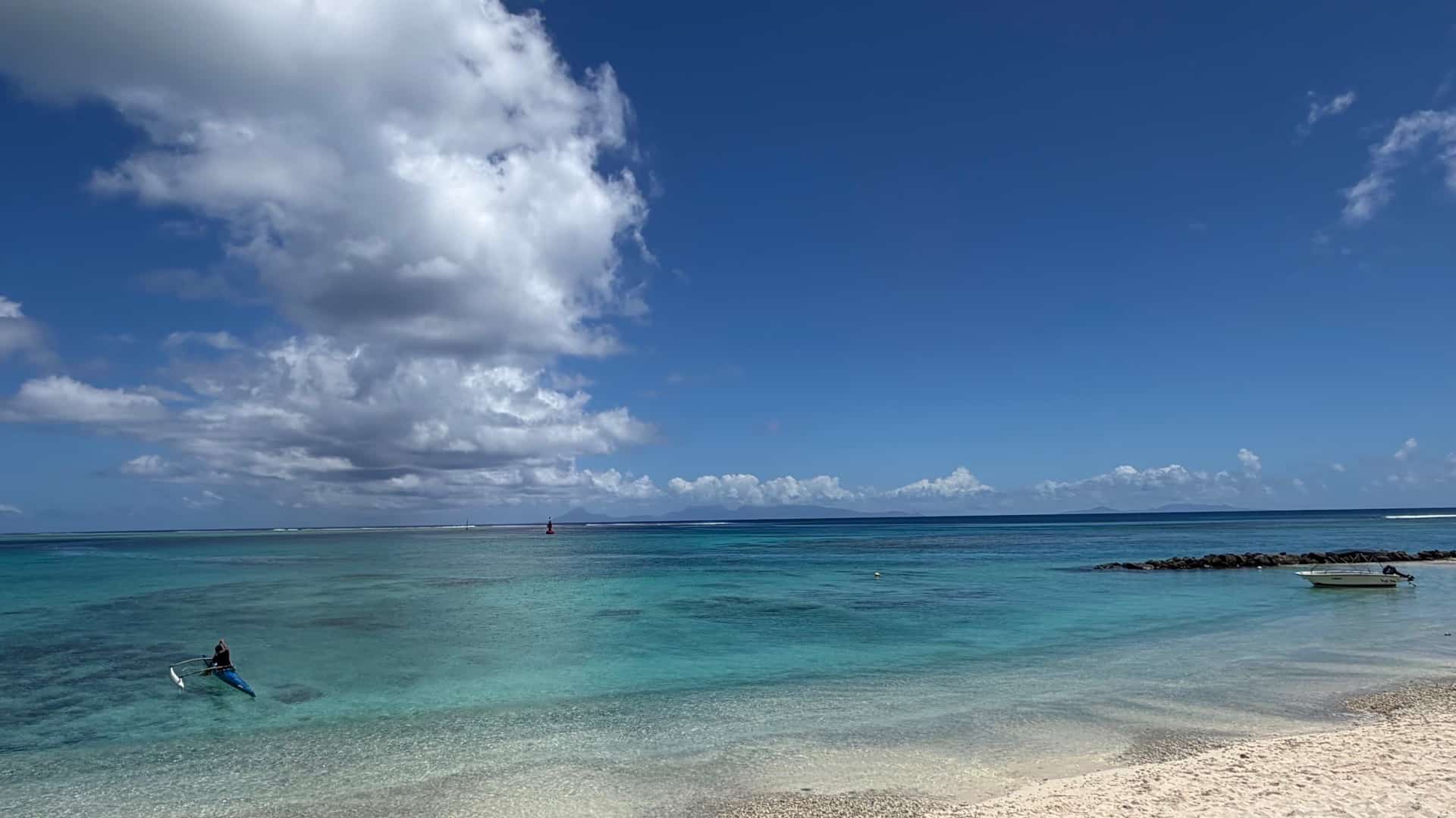 Outrigger canoe paddling across the calm turquoise waters of a scenic tropical beach.