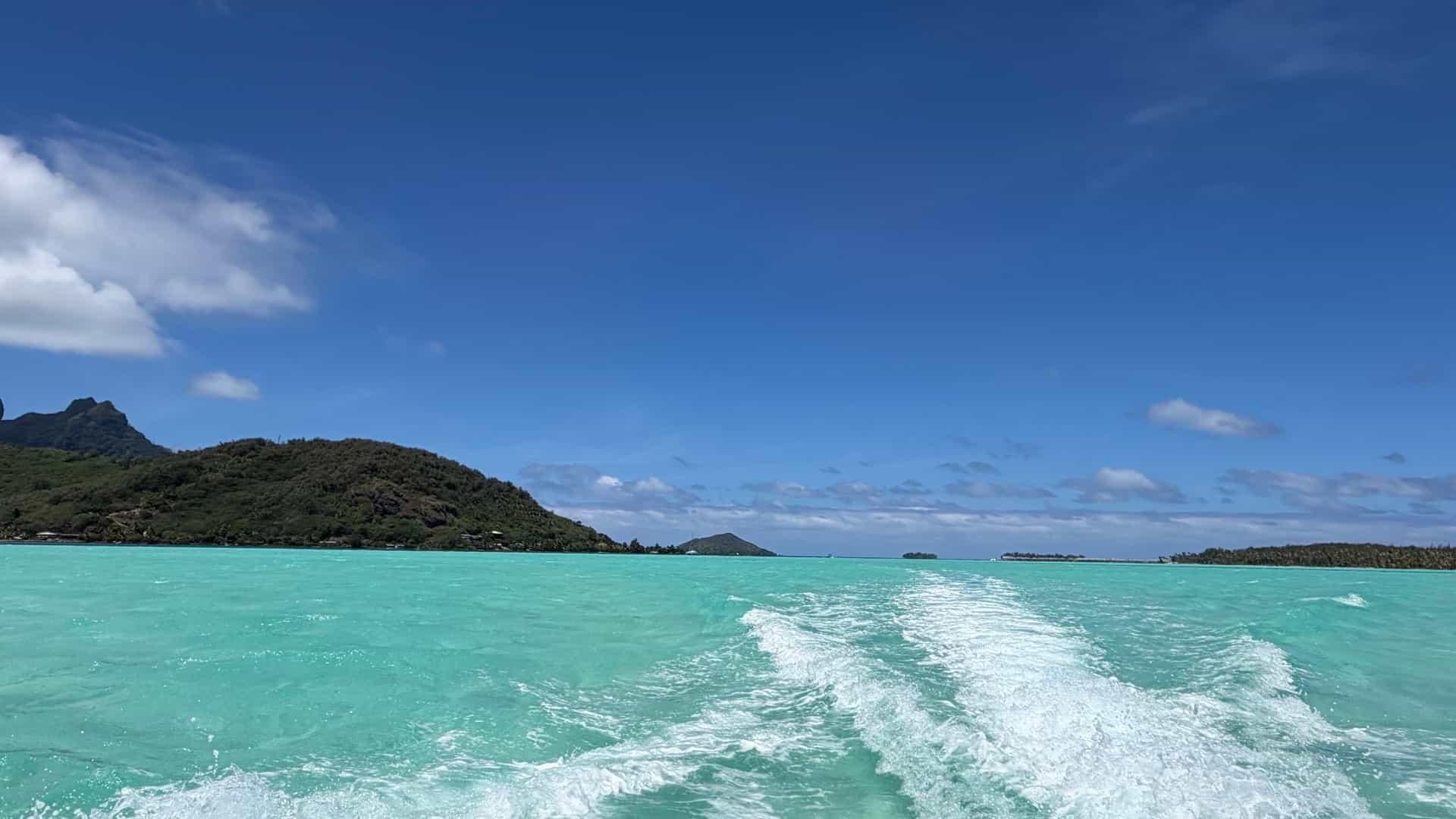 Motorboat creating white wakes across the shallow turquoise waters of a tropical lagoon.