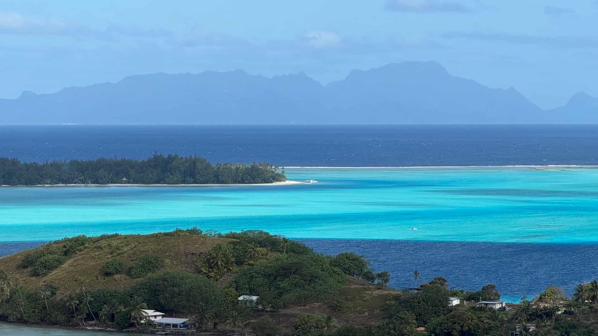Elevated view of lush green coastal hills overlooking turquoise lagoon waters and distant islands.