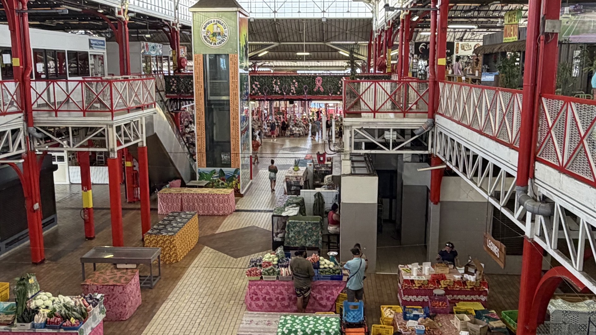 Central elevator tower and structural iron columns inside the bustling two-story Papeete municipal market.