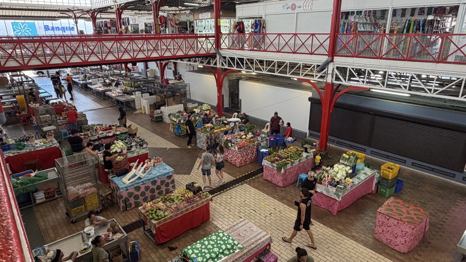 Interior view of the lower level showcasing various produce stalls and shoppers walking across tiled floors.