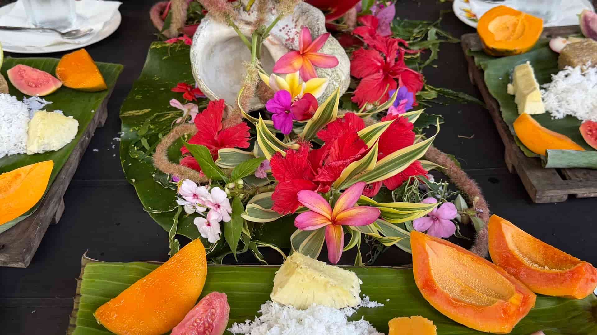 Traditional Polynesian table setting featuring fresh papaya, sliced guava, and grated coconut on banana leaves.
