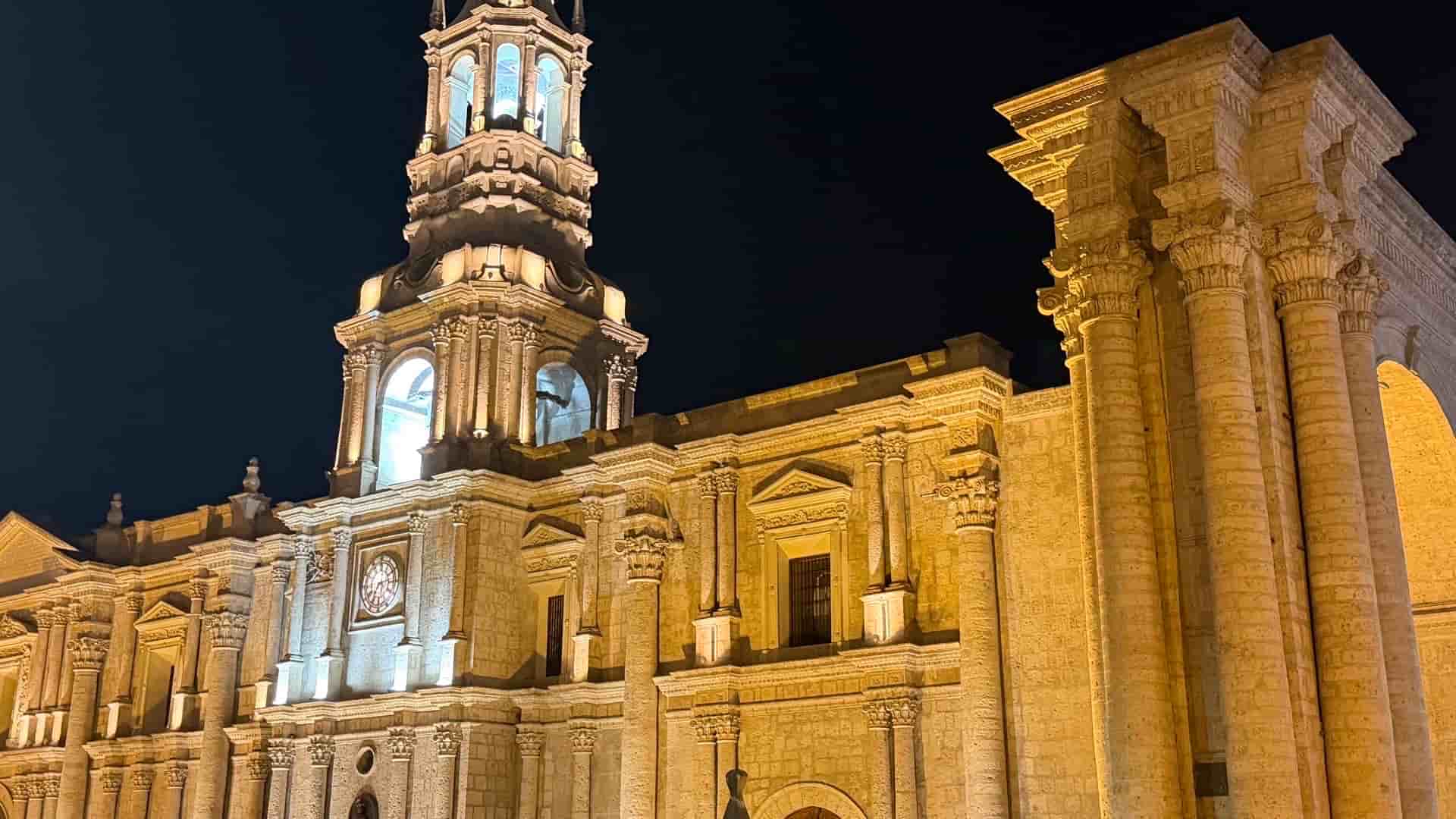 Illuminated stone facade and bell tower of Arequipa Cathedral glowing warmly against the night sky.