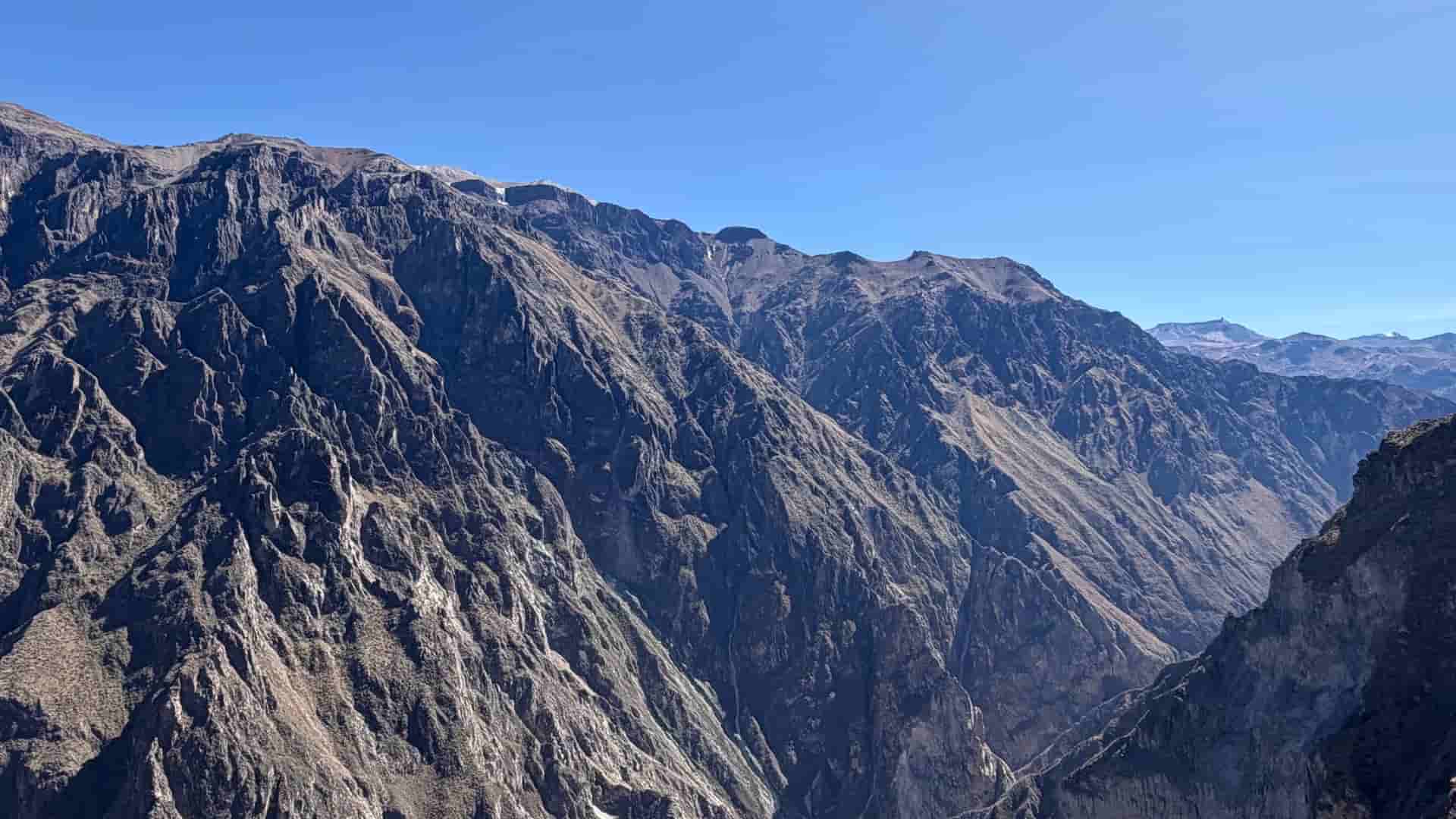 Vast expanse of steep, rocky canyon walls under a clear blue sky.