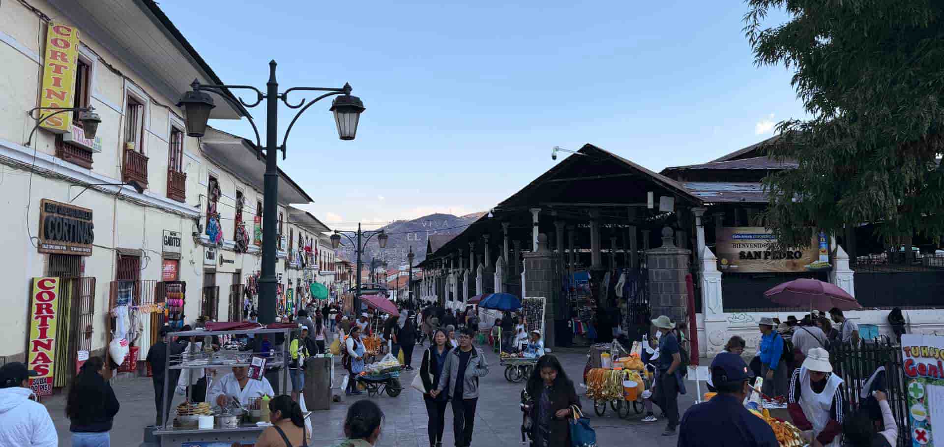 Crowded street and traditional storefronts outside the bustling San Pedro Market in Cusco.