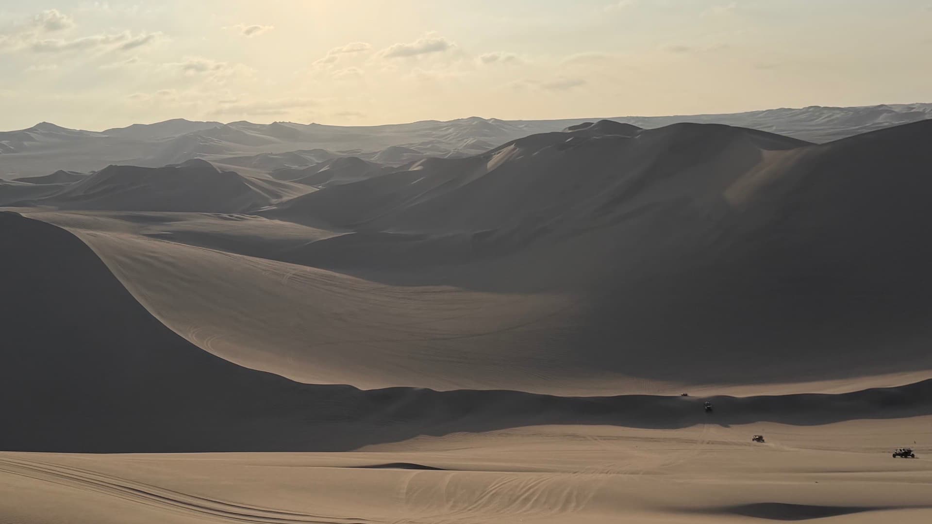 Sweeping panoramic view of vast golden desert sand dunes under a bright sunny sky.