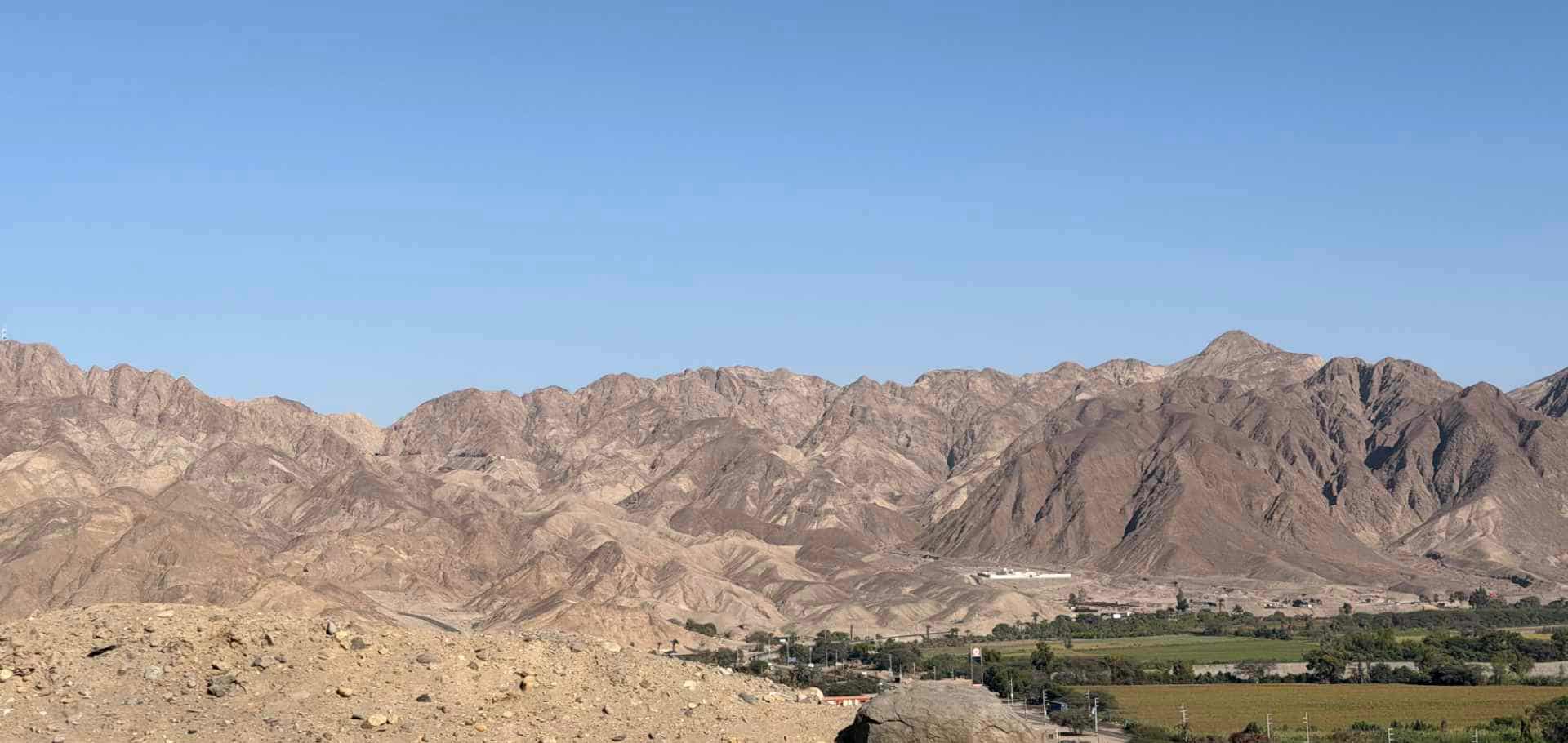 Rugged, arid mountain ranges under a clear blue sky near the Ica desert expanse.
