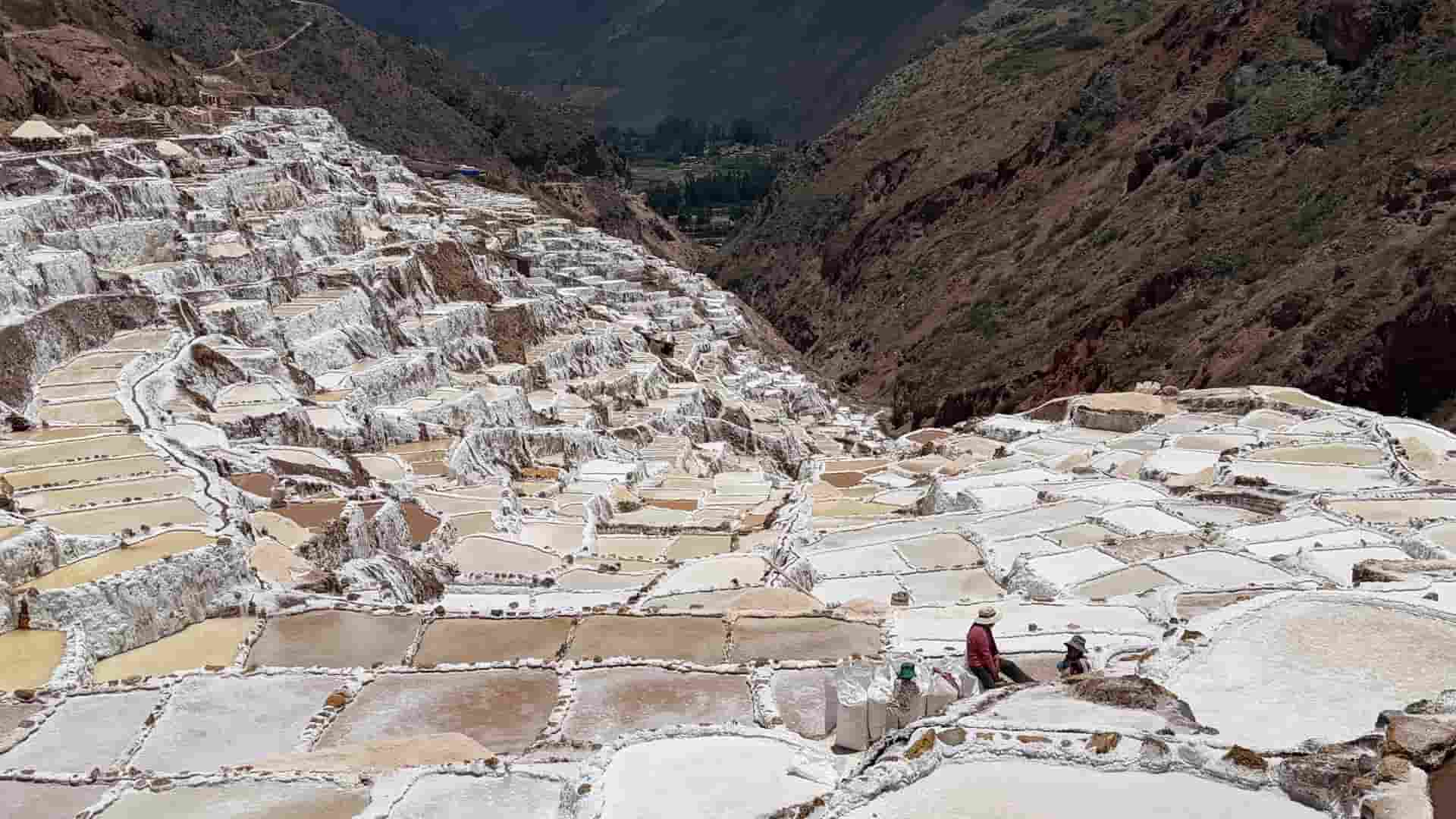 High-altitude view of terraced salt evaporation pools under a bright blue sky.