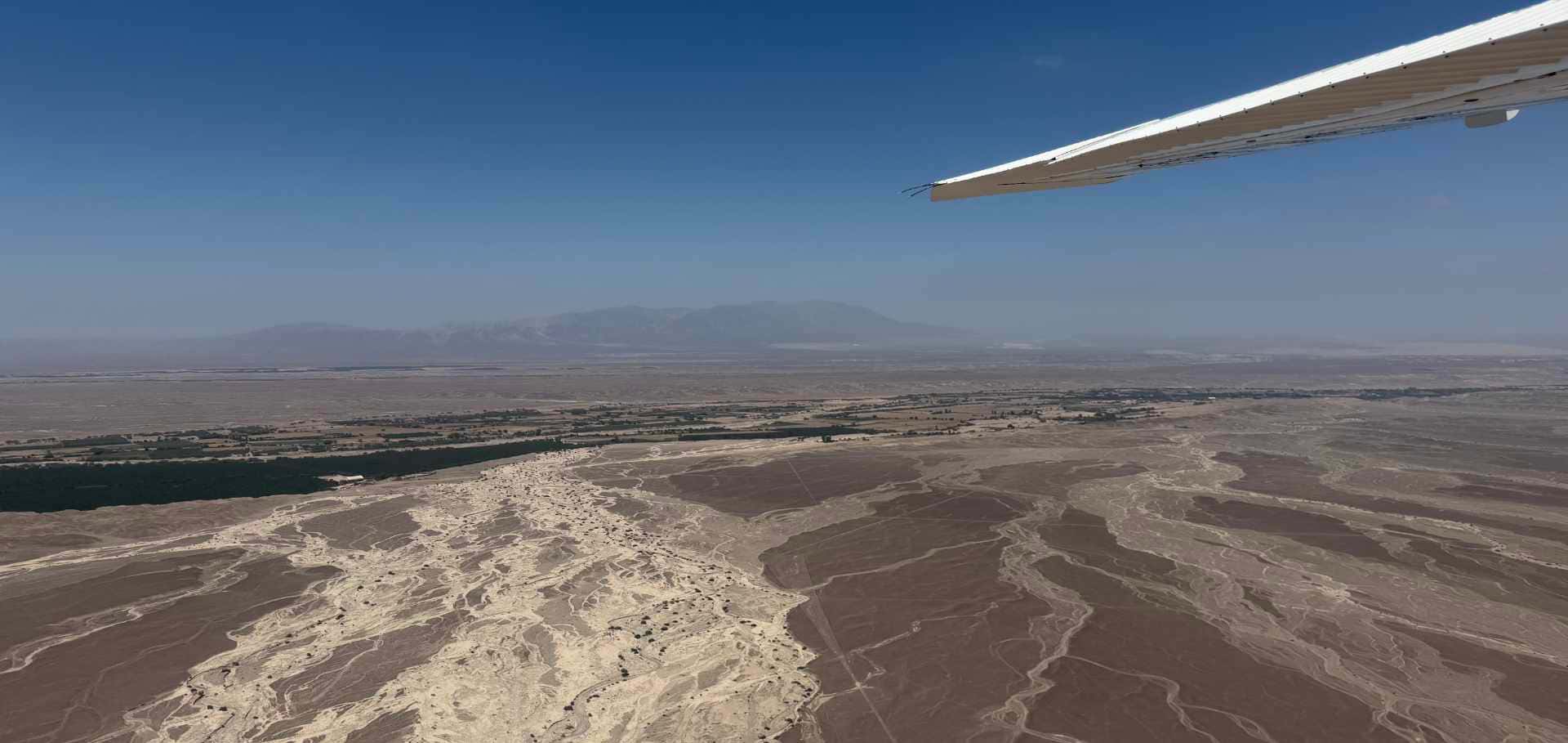 Airplane wing overlooking the sweeping desert terrain and distant mountain ranges of Nazca.