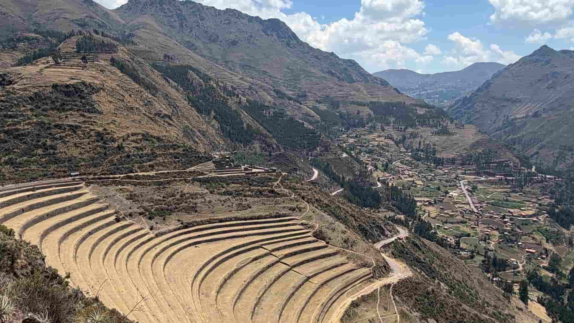 Agricultural terraces descending toward a valley village and winding mountain road.