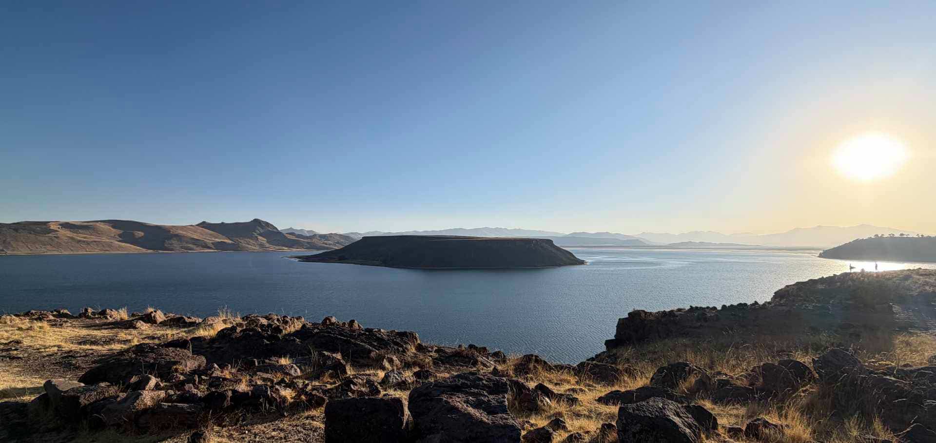 Expansive view of a large blue lake surrounded by rolling hills and bright sunlight.