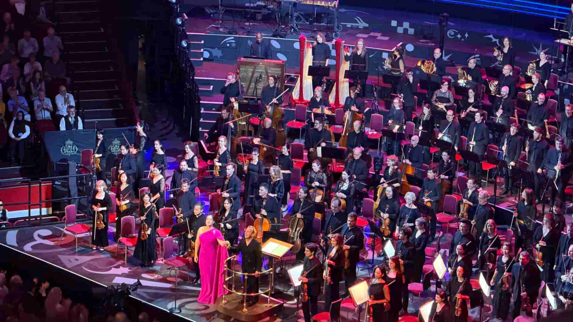 A soprano singer in a bright pink dress performing with the large orchestra on stage