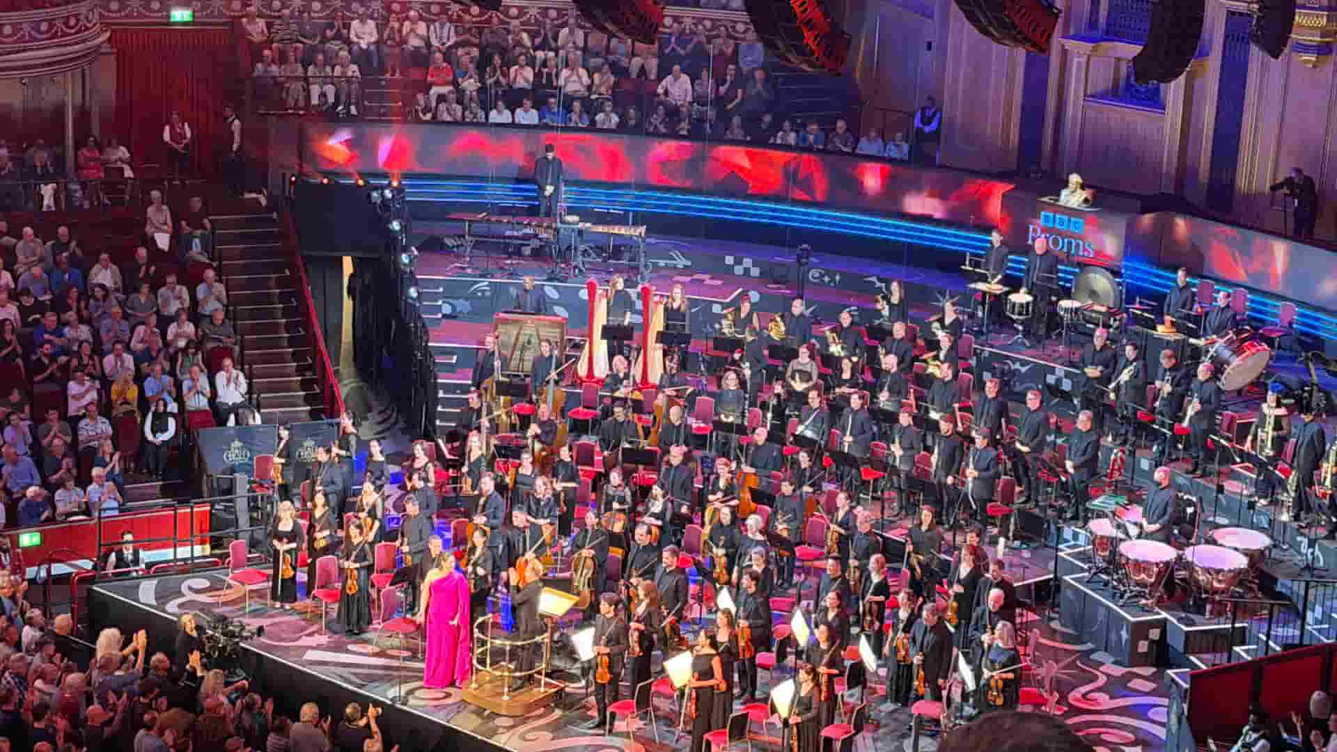 A soprano singer in a bright pink dress performing with the large orchestra on stage