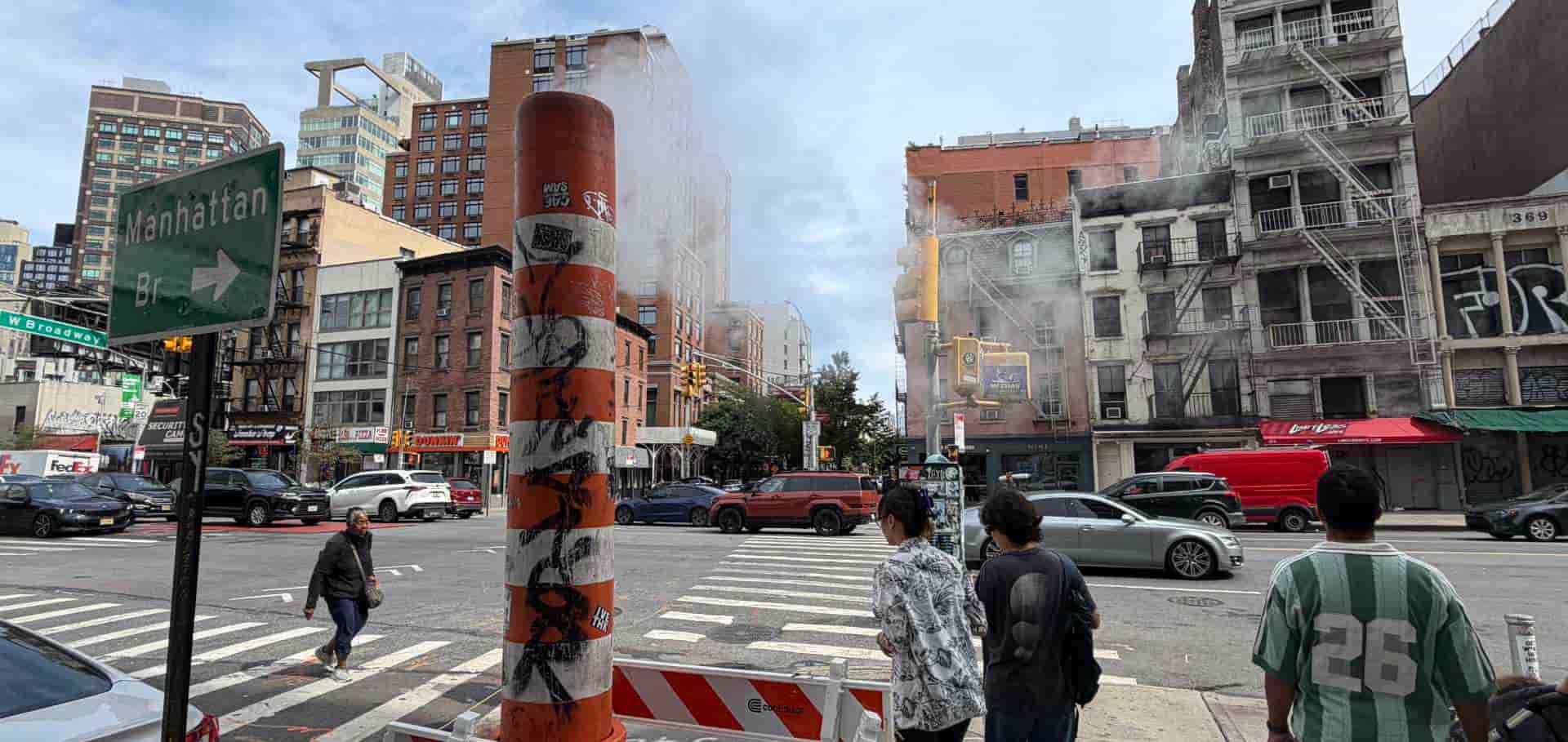 Striped orange and white steam release chimney standing on a busy New York City street corner