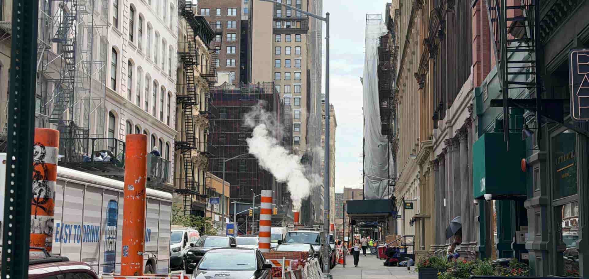 White steam venting from a utility stack on a dense Manhattan street surrounded by historic buildings
