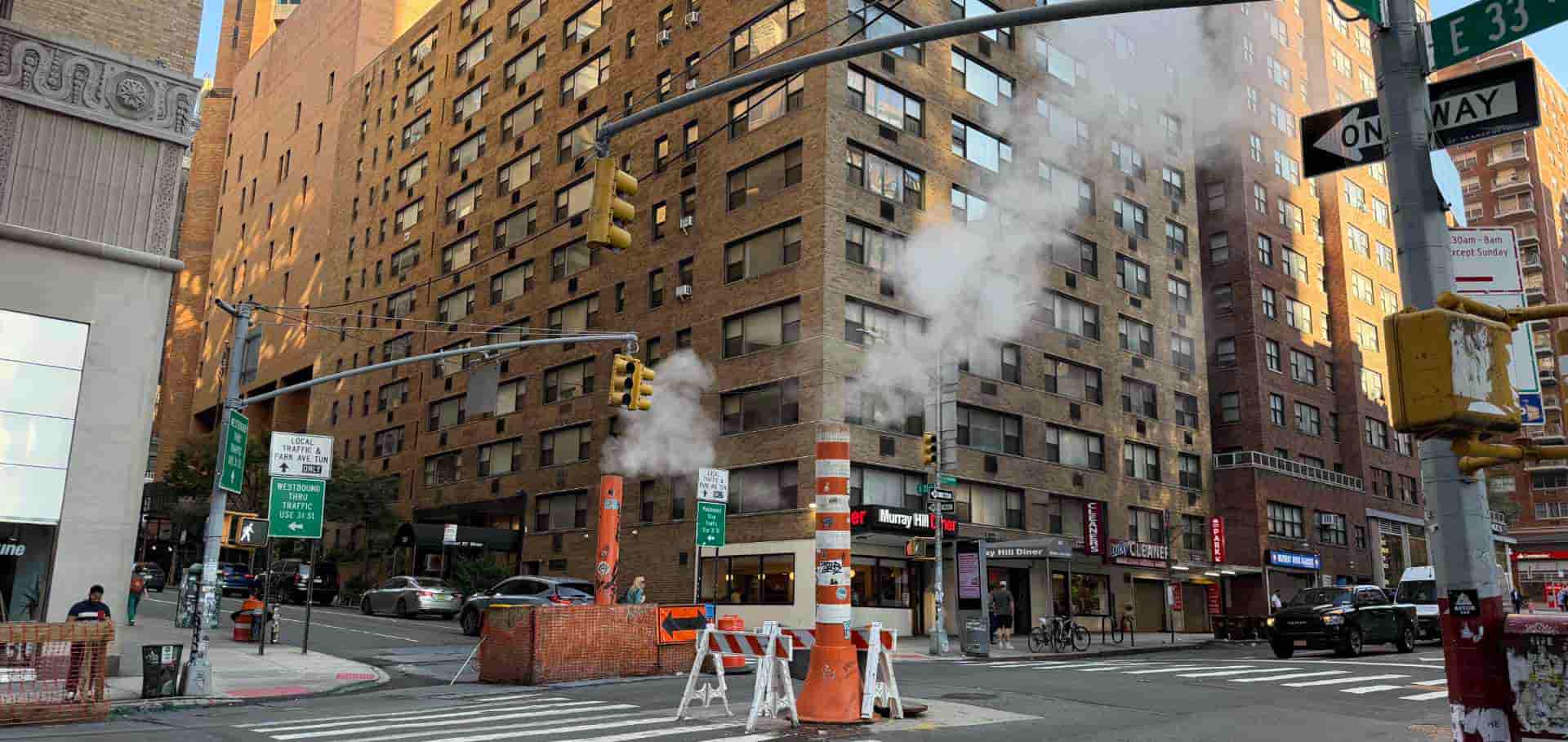 Striped orange steam pipe and construction barriers on a busy street corner in Manhattan