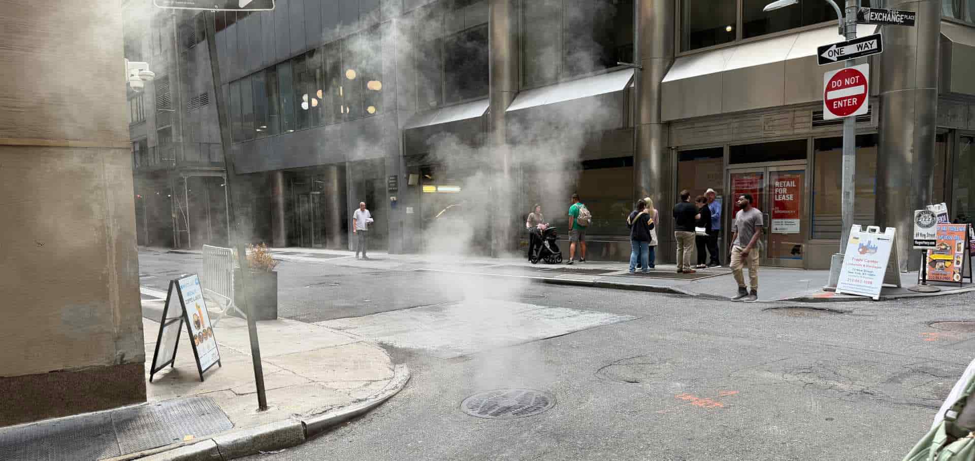 Pedestrians walking past billowing steam rising from the pavement in lower Manhattan
