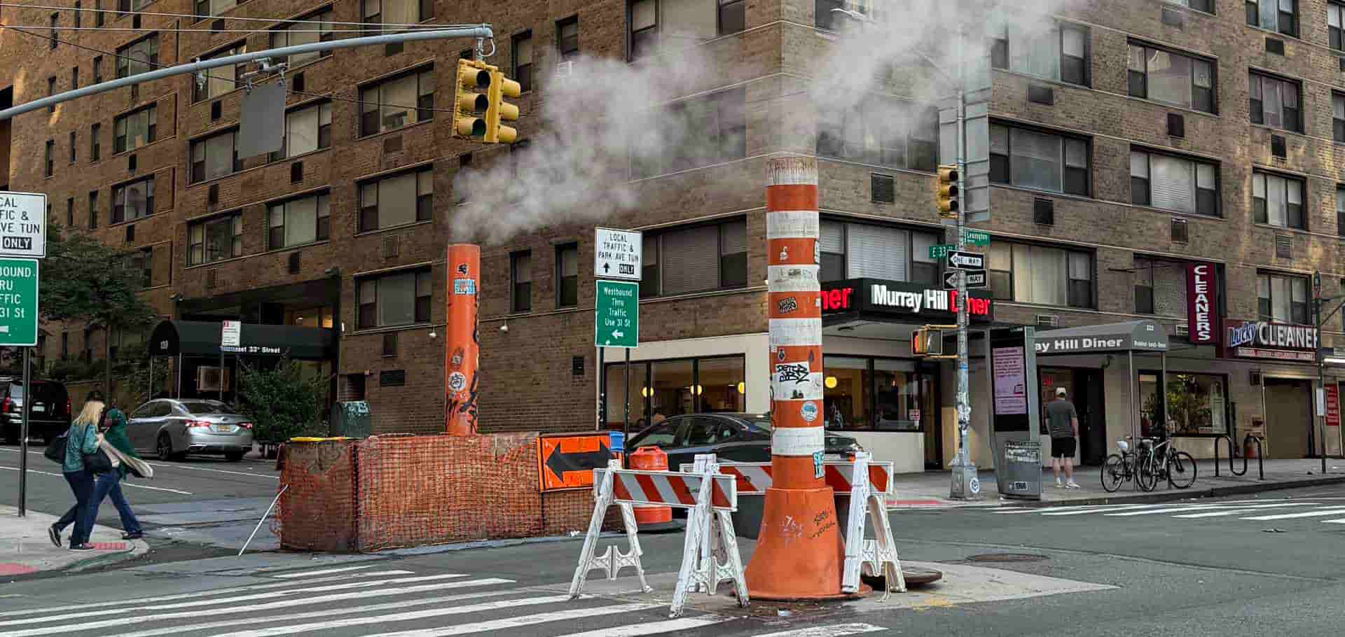 Striped orange steam pipe and construction barriers on a busy street corner in Manhattan