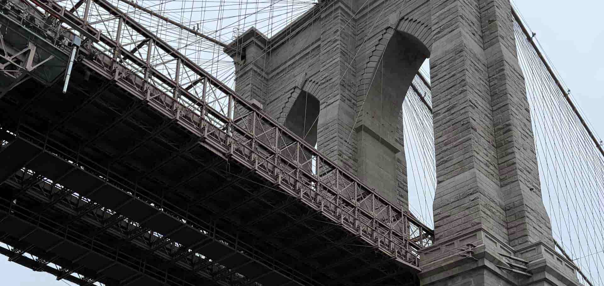 Low angle shot of the historic stone pier arch and suspension trusses of the Brooklyn Bridge.
