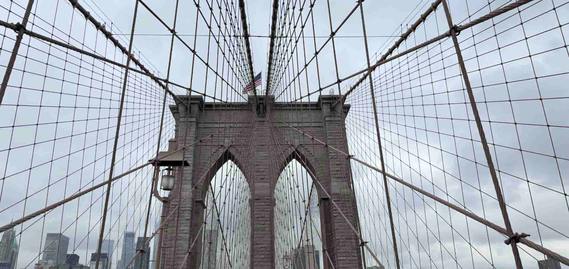 Low angle view of the massive stone towers and complex steel suspension cables of the Brooklyn Bridge.