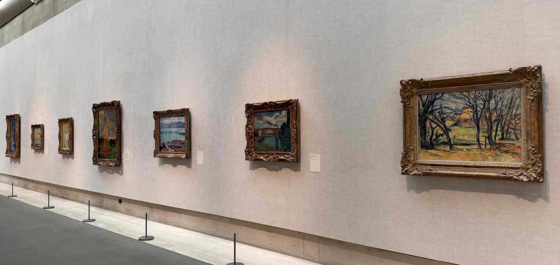 Impressionist landscape paintings displayed along a minimalist white exhibition wall.