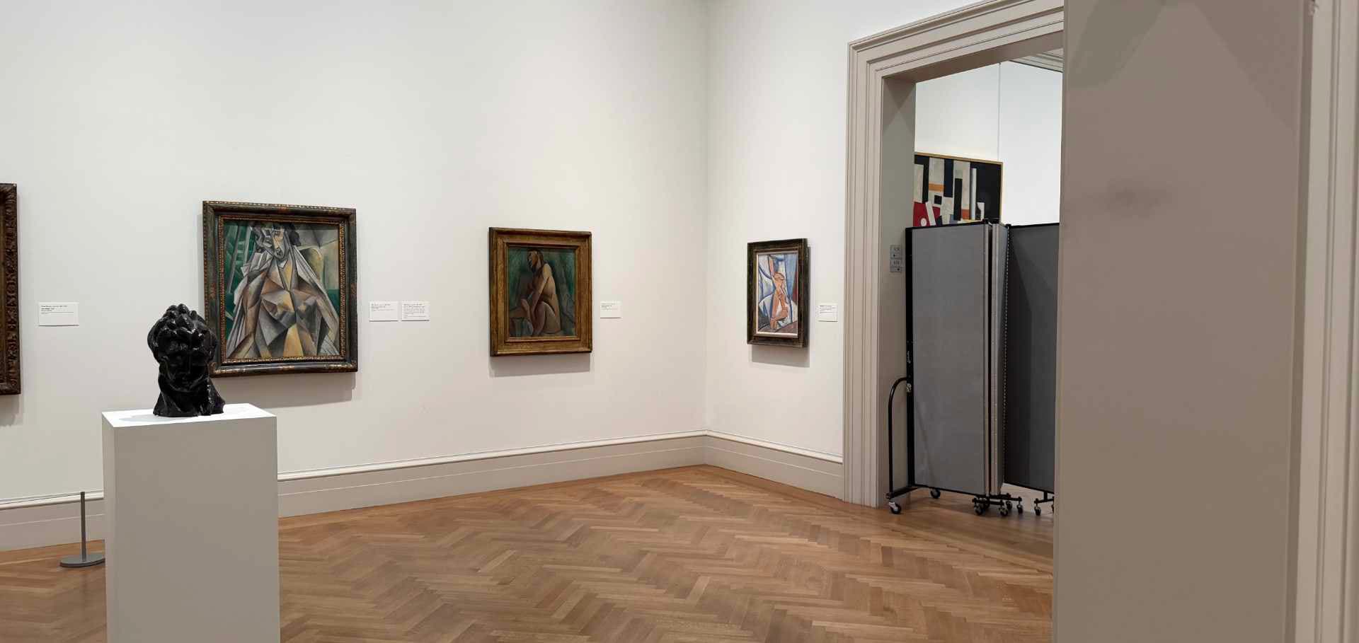 Modernist paintings and a bronze sculpture displayed inside the bright exhibition galleries of the museum