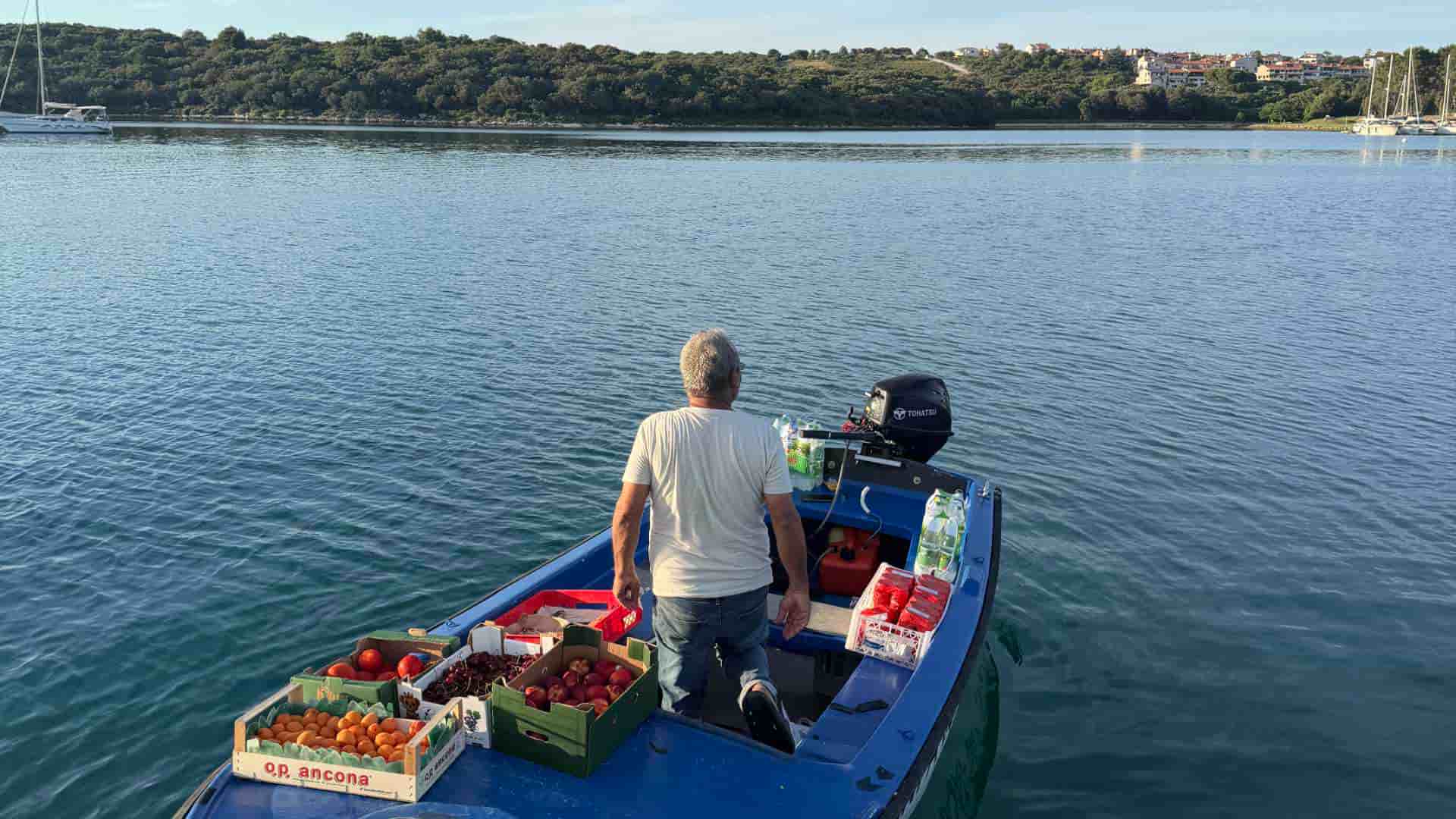 Suleiman stands in his blue wooden boat loaded with fresh fruit and water in Soline Bay