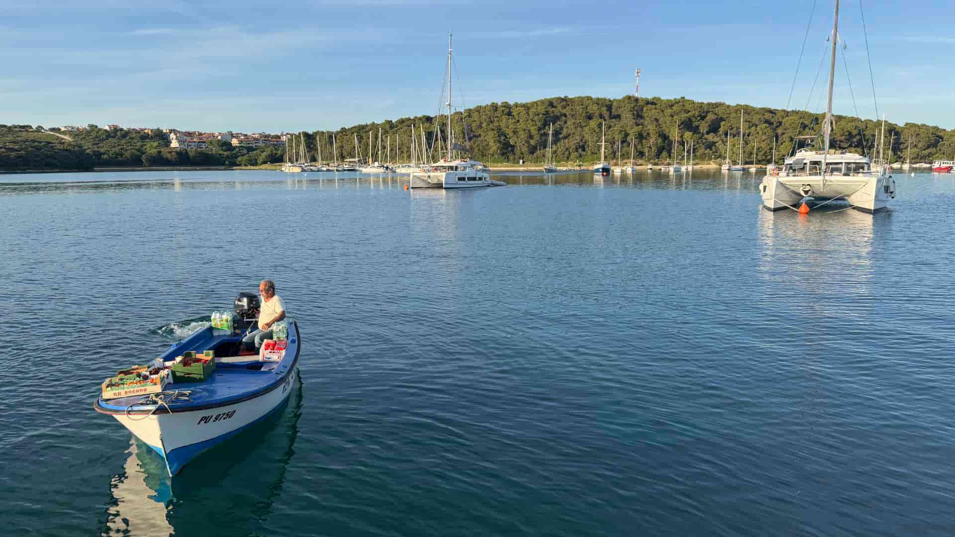 A traditional blue motorboat navigates past luxury yachts anchored in the calm waters of Istria
