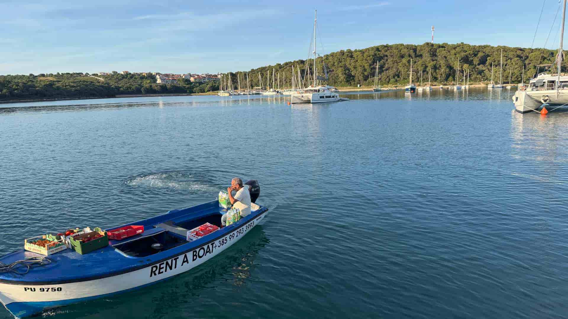 Suleiman operates his blue supply boat past luxury catamarans anchored in Soline Bay